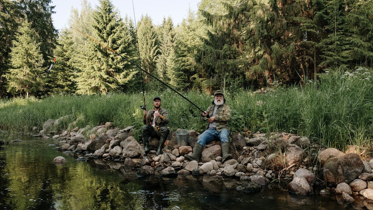 Two men are fishing by a serene river surrounded by lush greenery. Perfect capturing of nature and leisure.